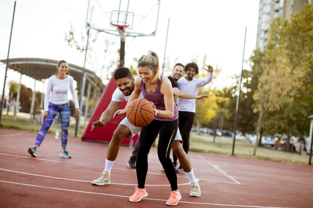 Group of multiracial young people playing basketball outdoors