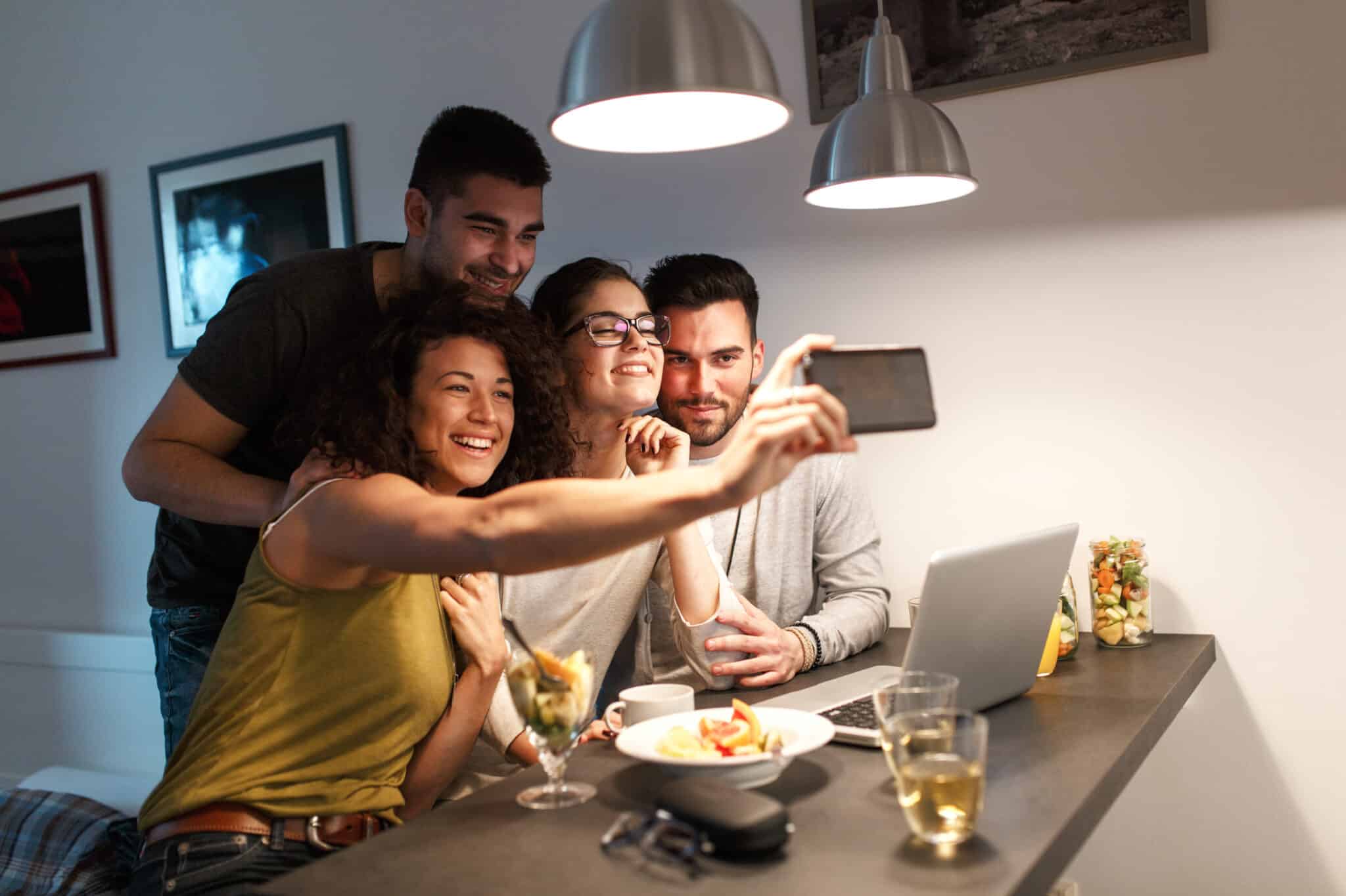 Friends sitting together in living room and watching movie on on laptop and taking selfie